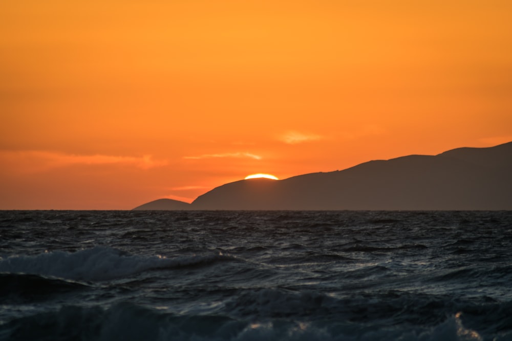 a sunset over the ocean with a small island in the distance