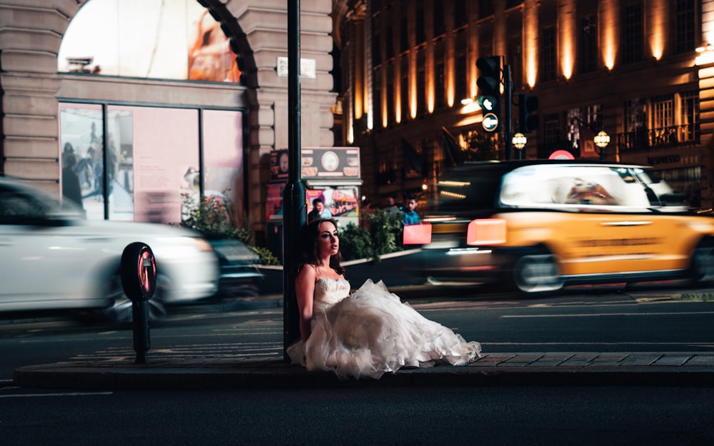 a woman in a wedding dress is sitting on a street corner