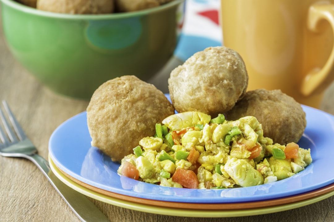 a blue plate topped with food next to a cup of coffee, Jamaican ackee and saltfish served with a side of fried dumplings