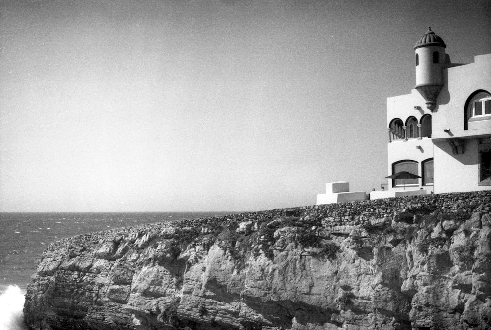 a black and white photo of a lighthouse on a cliff