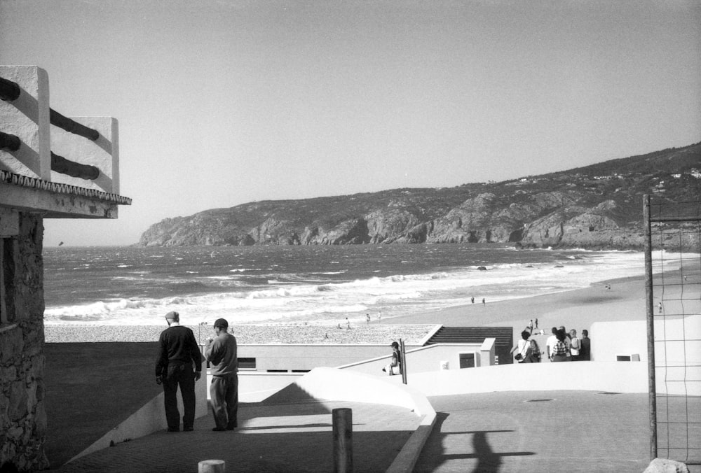 a black and white photo of two men walking towards the beach