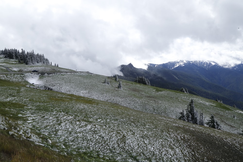 ein grasbewachsenes Feld mit Schnee auf dem Boden und Bergen im Hintergrund