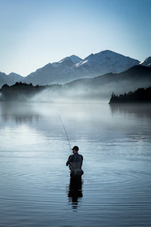 A fisherman casting a line into a misty mountain lake at sunrise.
