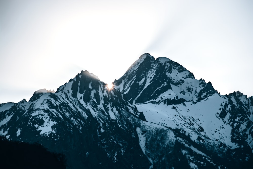 Una montaña cubierta de nieve con el sol brillando a través de las nubes