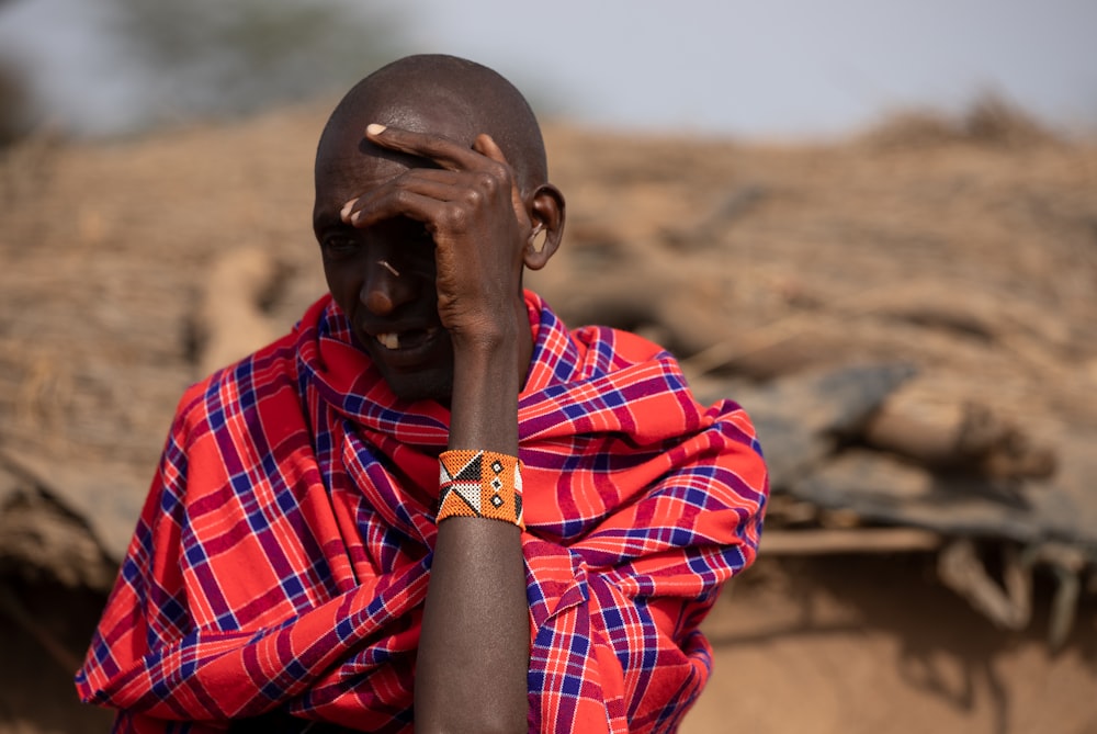 a man in a red and blue checkered shirt holds his hand to his face