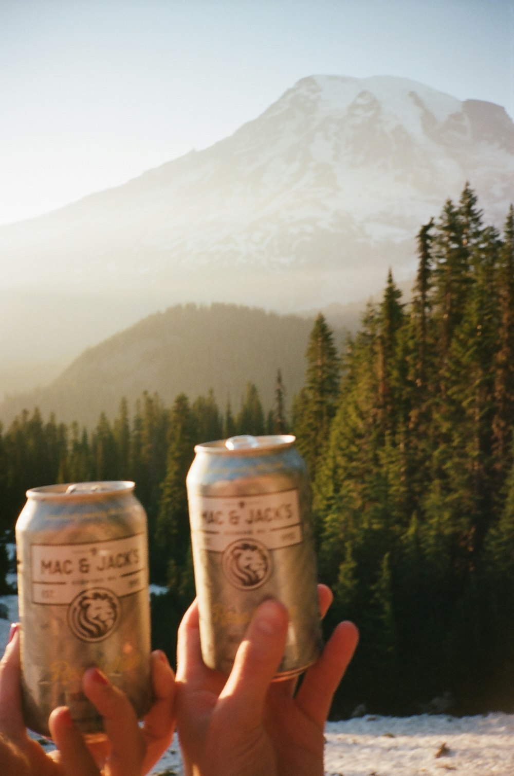 a person holding two cans of beer in front of a mountain