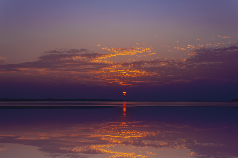 the sun is setting over the water with clouds in the sky