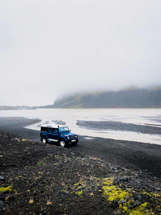a blue truck driving down a road next to a body of water