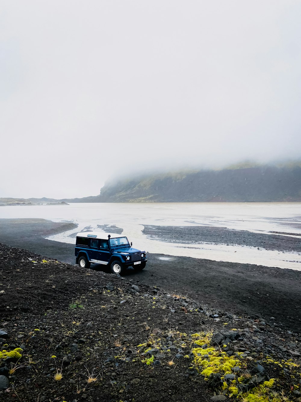 a blue truck driving down a road next to a body of water