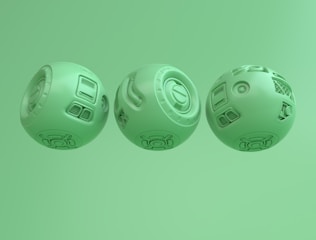 Three spherical objects displaying intricate mechanical designs with various panels and patterns. Each sphere has distinct elements such as vents, circular motifs, and geometric engravings. The objects are uniformly colored light green and arranged side by side against a matching green background.
