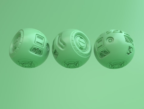 Three spherical objects displaying intricate mechanical designs with various panels and patterns. Each sphere has distinct elements such as vents, circular motifs, and geometric engravings. The objects are uniformly colored light green and arranged side by side against a matching green background.