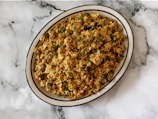 A plate of scrambled tofu with vegetables is placed on a marbled surface. The dish contains a mix of crumbled tofu, green bell peppers, onions, and possibly spices, creating a colorful and textured appearance.
