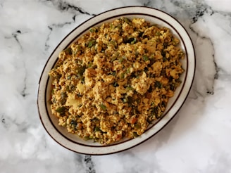 A plate of scrambled tofu with vegetables is placed on a marbled surface. The dish contains a mix of crumbled tofu, green bell peppers, onions, and possibly spices, creating a colorful and textured appearance.