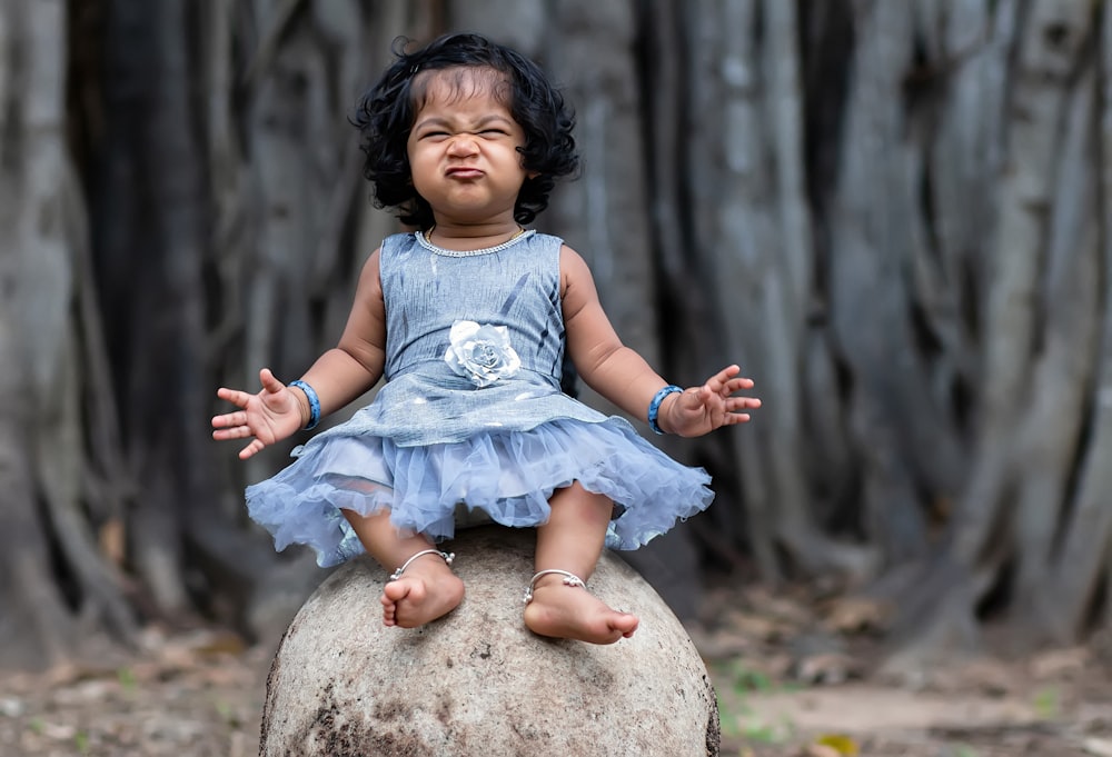 a little girl sitting on top of a rock