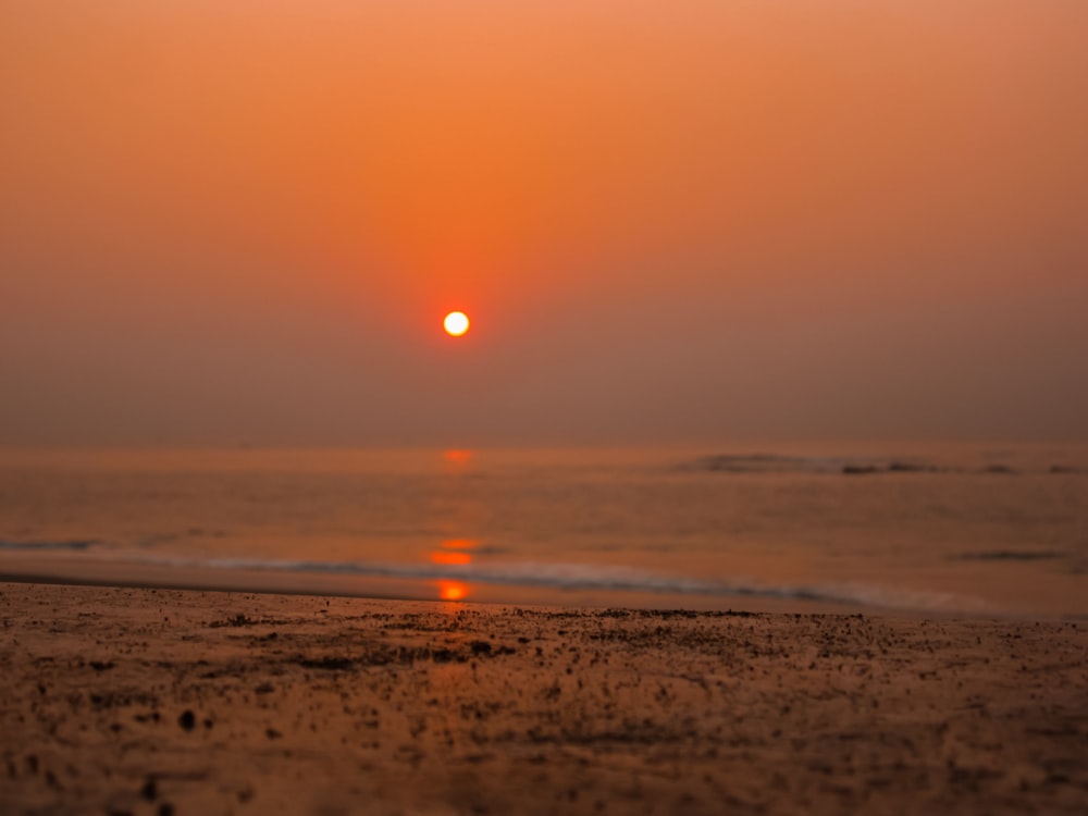 the sun is setting over the water on the beach