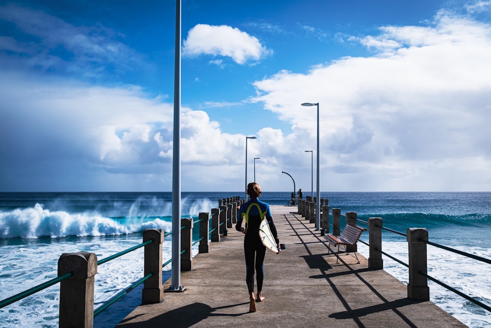 a man walking down a pier holding a surfboard