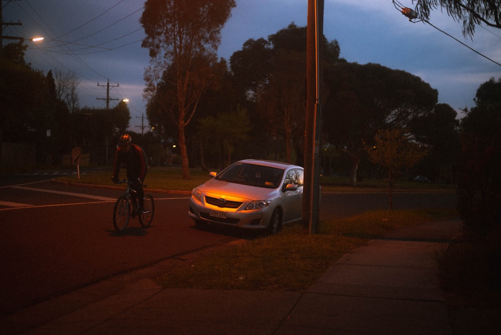 um homem andando de bicicleta por uma rua ao lado de um carro