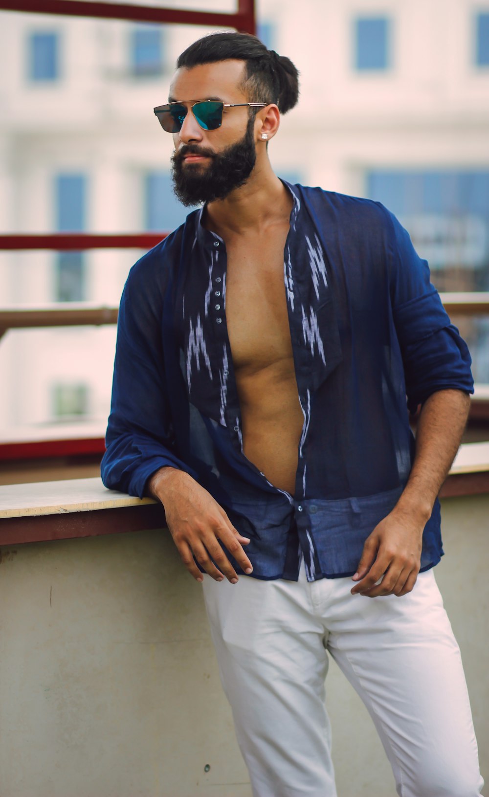 a man with a beard wearing sunglasses leaning against a wall