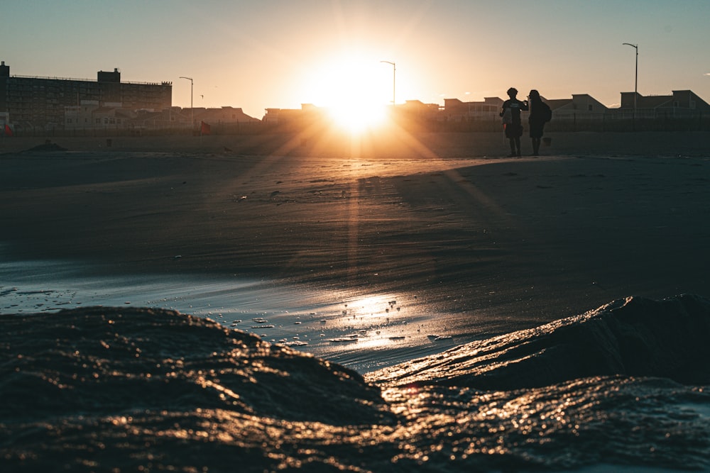 a couple of people standing on top of a sandy beach