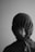 A person is wearing a hoodie with the hood tightened around their face, obscuring most features except for the eyes, nose, and part of the mouth. The monochrome setting adds a dramatic and mysterious feel.