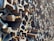 A large pile of rusty, weathered steel beams stacked in an interlocking pattern creating a complex, geometric texture. The light casts shadows, enhancing the rough surfaces and edges of the beams.