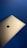 A sleek, silver laptop with a prominent black apple logo on its lid is positioned against a solid blue background. The contrast between the metallic finish of the laptop and the deep blue backdrop creates a striking composition.