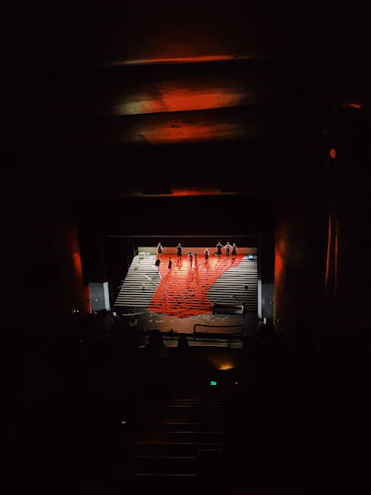 A dramatic theatrical stage with deep shadows, vibrant red accents, and elegant lighting highlighting performers.