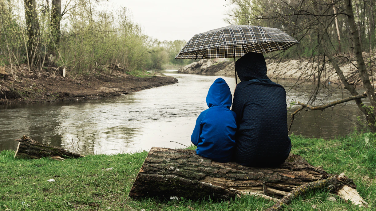 a couple of people sitting on a log under an umbrella