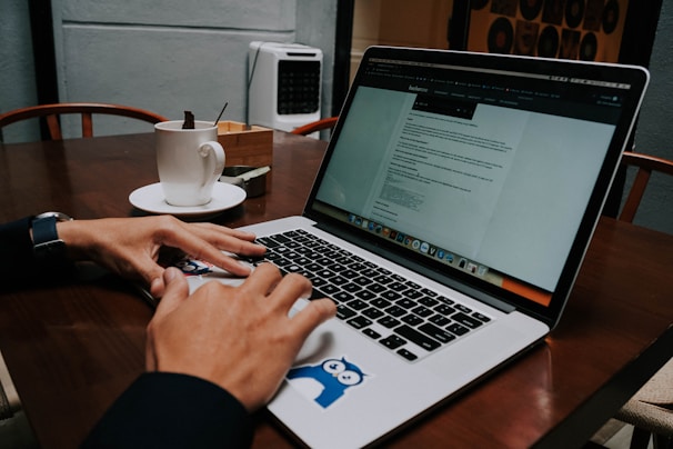 Person typing on laptop with a coffee cup nearby and workflow charts on the screen.