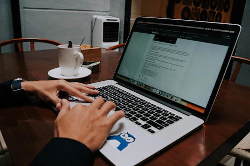 A friendly person typing on a laptop with a coffee cup nearby, symbolizing approachable support.