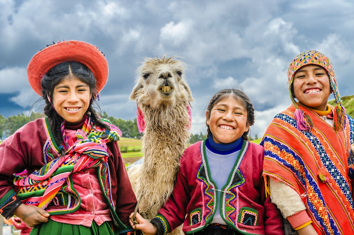 Cusco February — Peruvian women in traditional colourful dress with a llama against an Andean sky