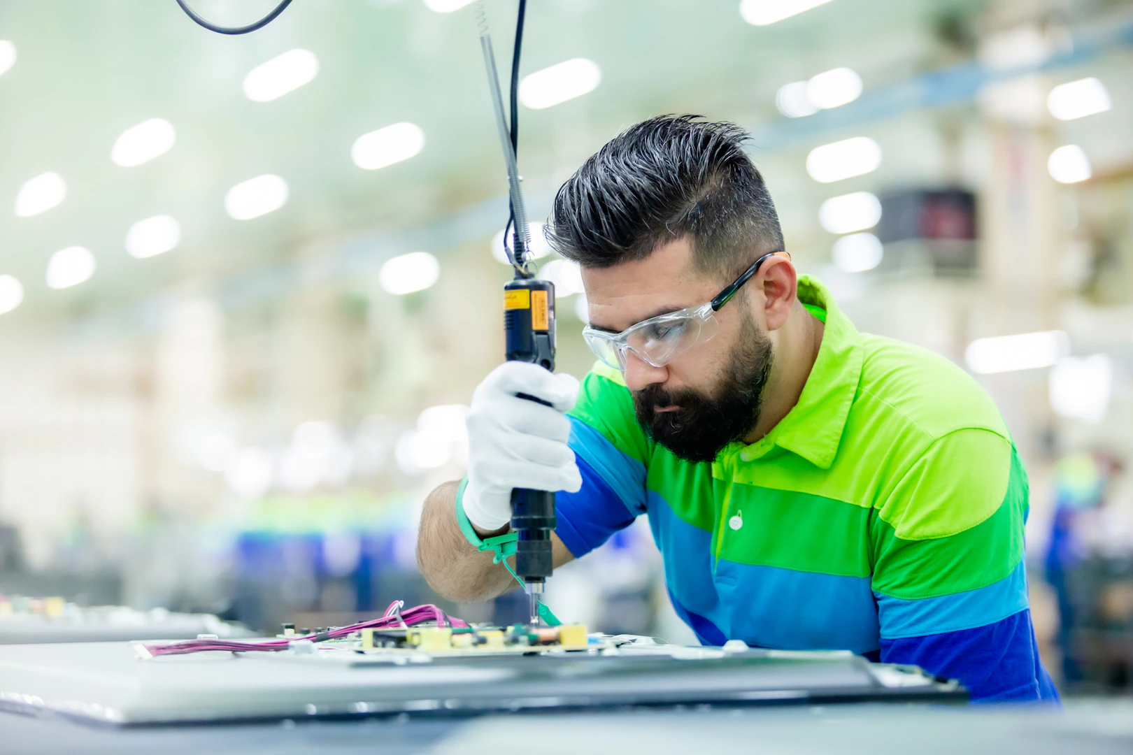 A technician wearing safety glasses assembling equipment in a factory