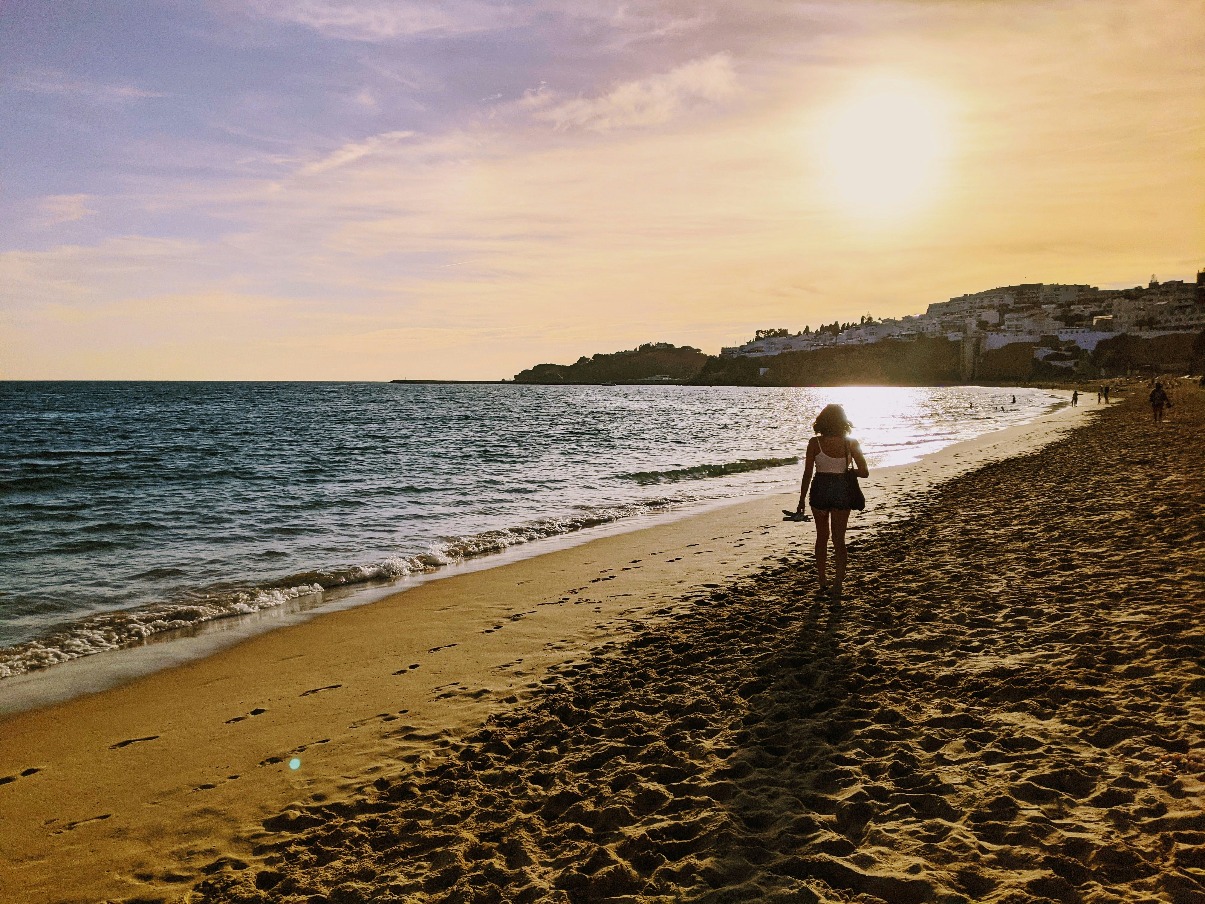 A woman walking along a beach next to the ocean photo – Free Background ...