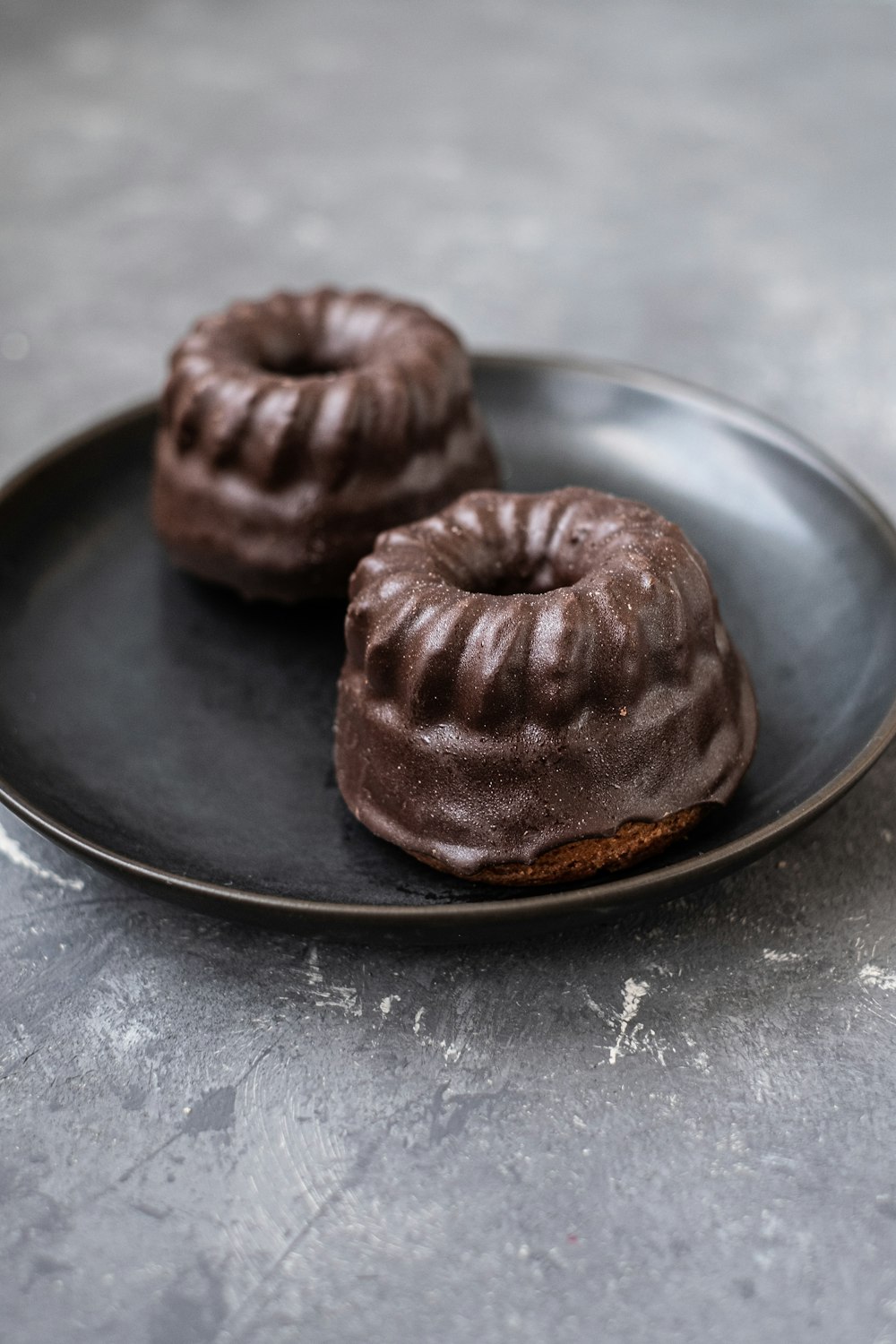 two chocolate donuts sitting on a black plate