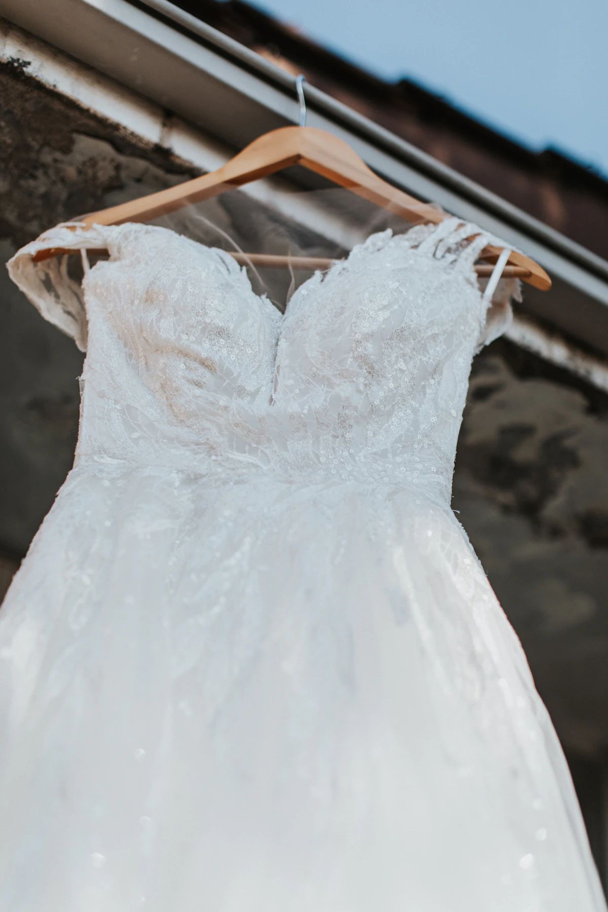 A white wedding dress hanging on a wooden hanger before the ceremony