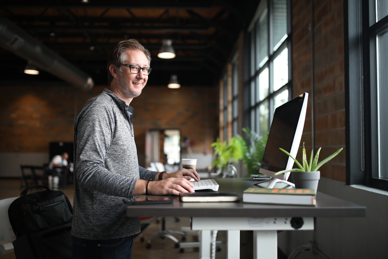A freelancer working at a standing desk by a window in a bright co-working space