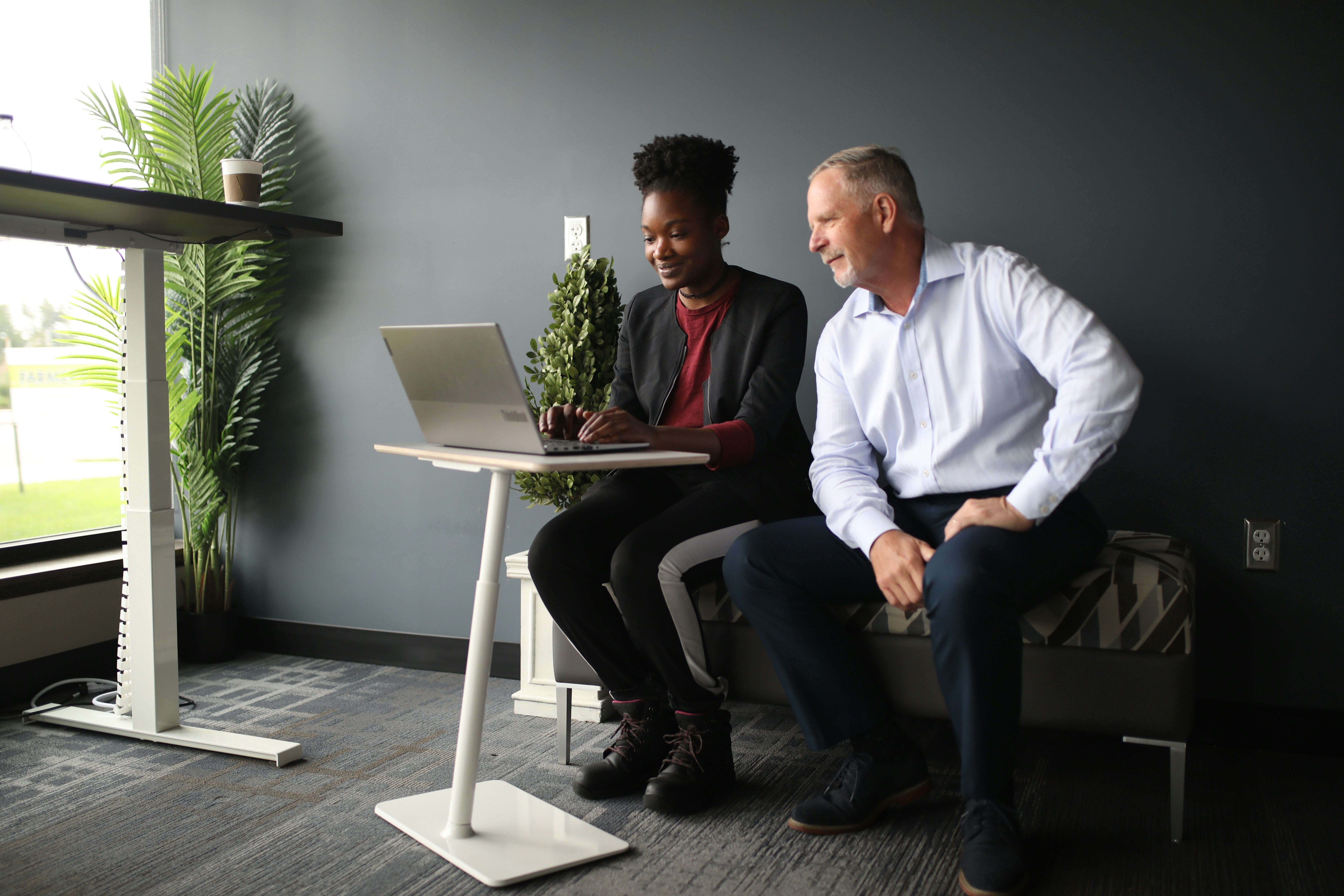 a man and a woman sitting on a bench looking at a laptop