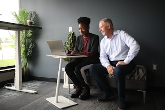 a man and a woman sitting on a bench looking at a laptop
