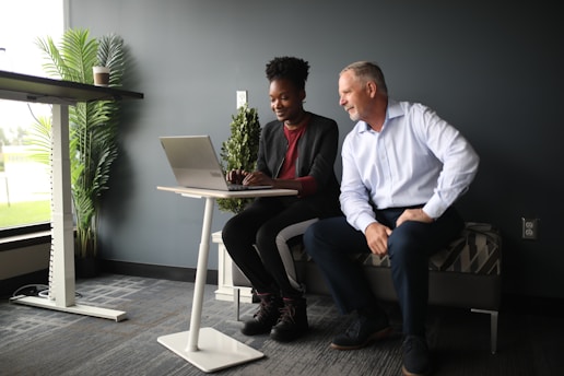 a man and a woman sitting on a bench looking at a laptop