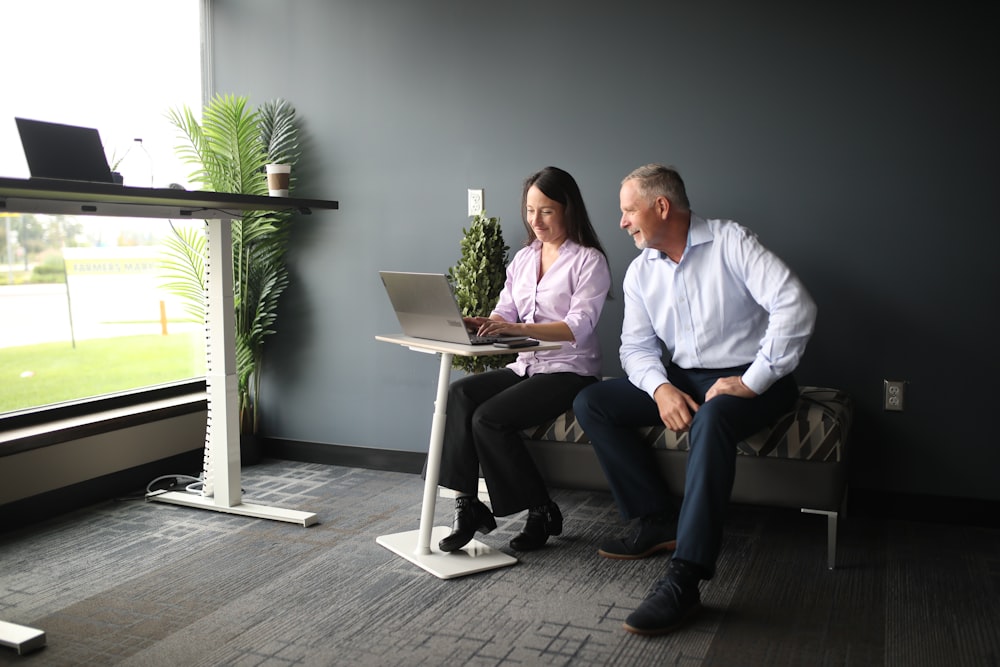 a man and a woman sitting on a bench looking at a laptop