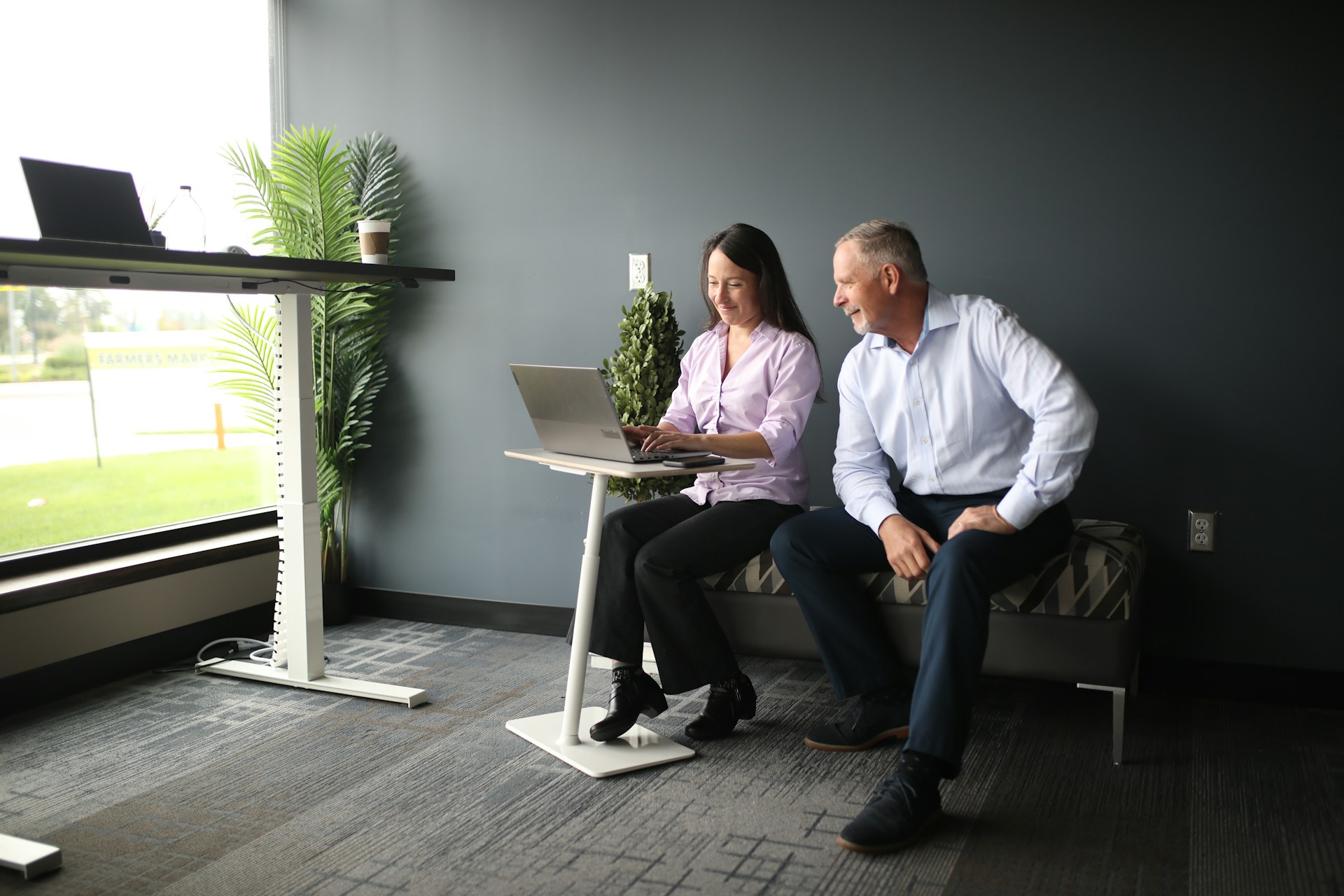 a man and a woman sitting on a bench looking at a laptop