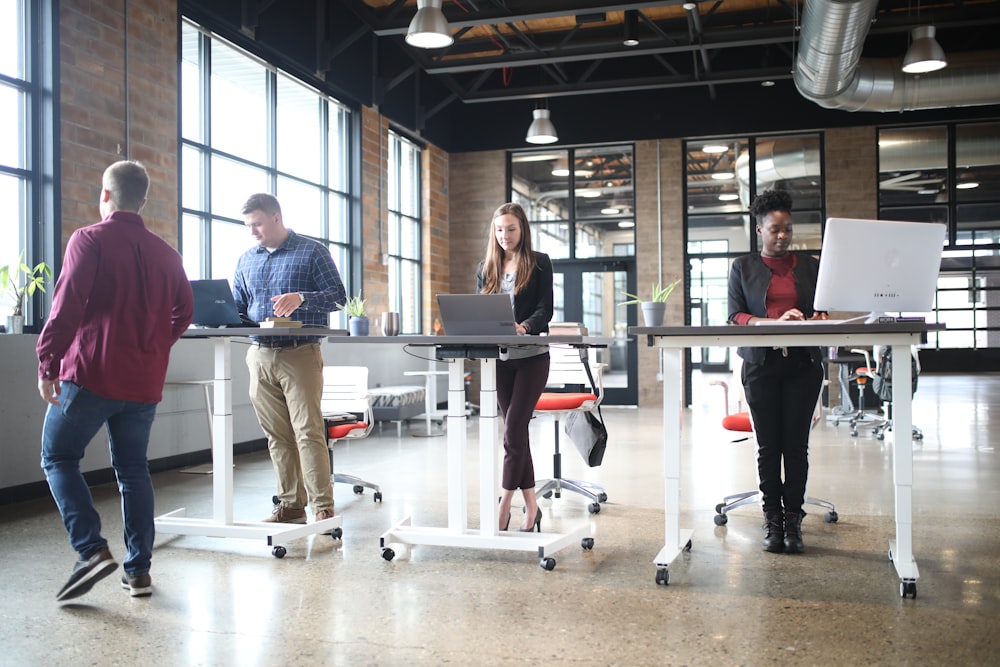 a group of people standing around a table with laptops