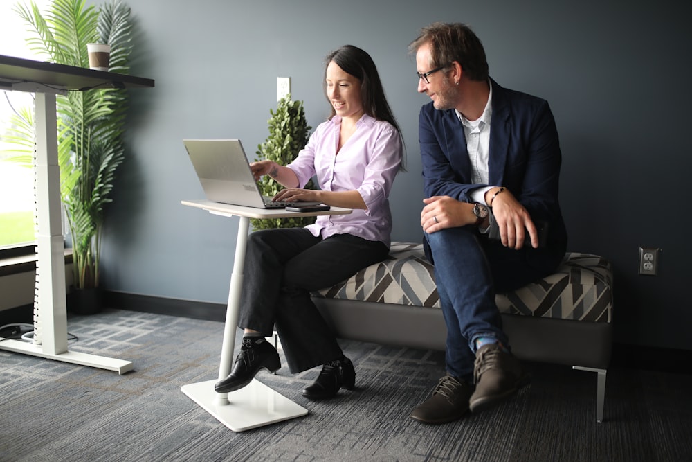 a man and a woman sitting on a bed looking at a laptop