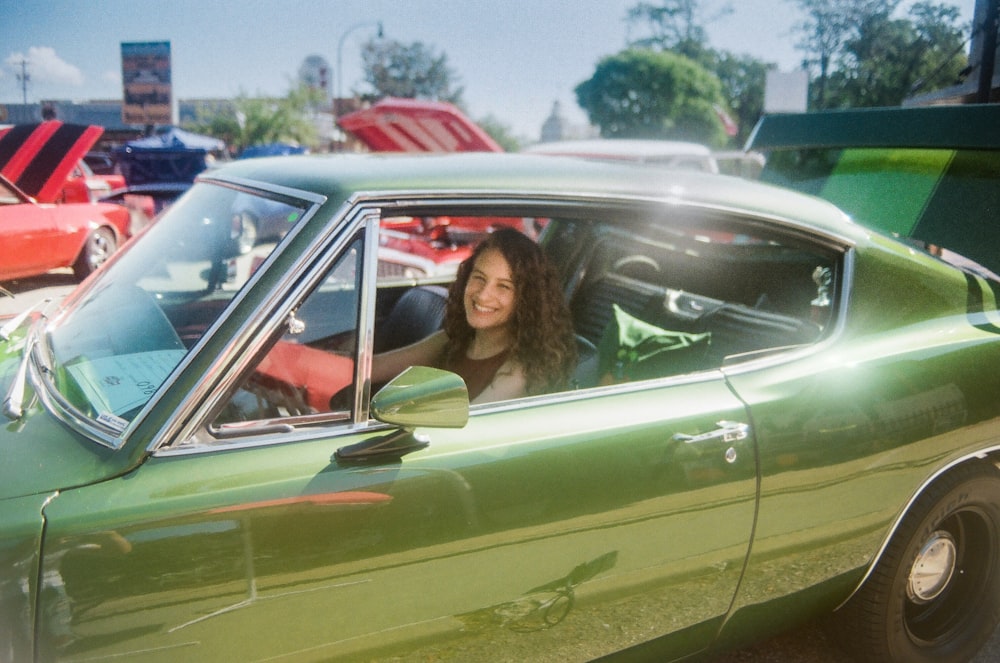 a woman sitting in a green car in a parking lot