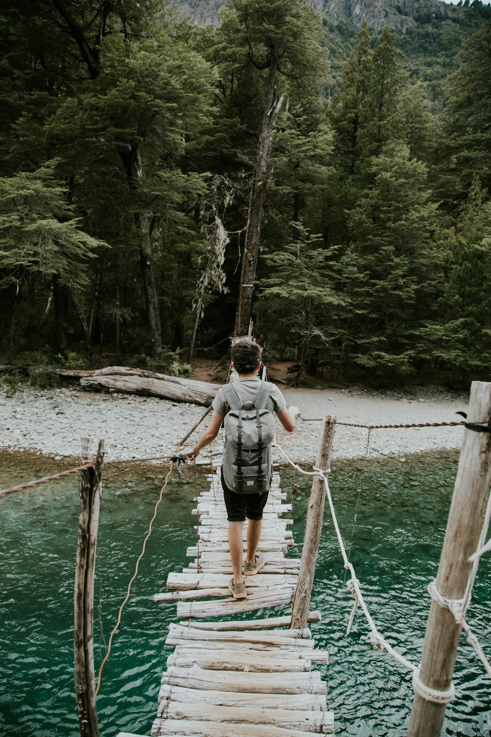 a man walking across a wooden bridge over a river