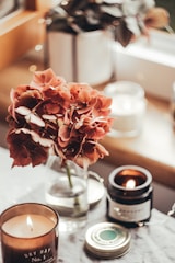 Cozy artisan candle and floral arrangement setup with soft natural lighting on a wooden table.