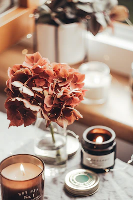 A cozy candle glowing softly on a wooden table surrounded by dried flowers