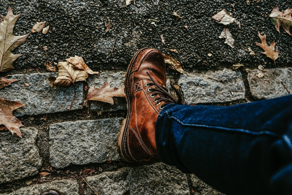 a person wearing brown shoes standing next to a brick wall
