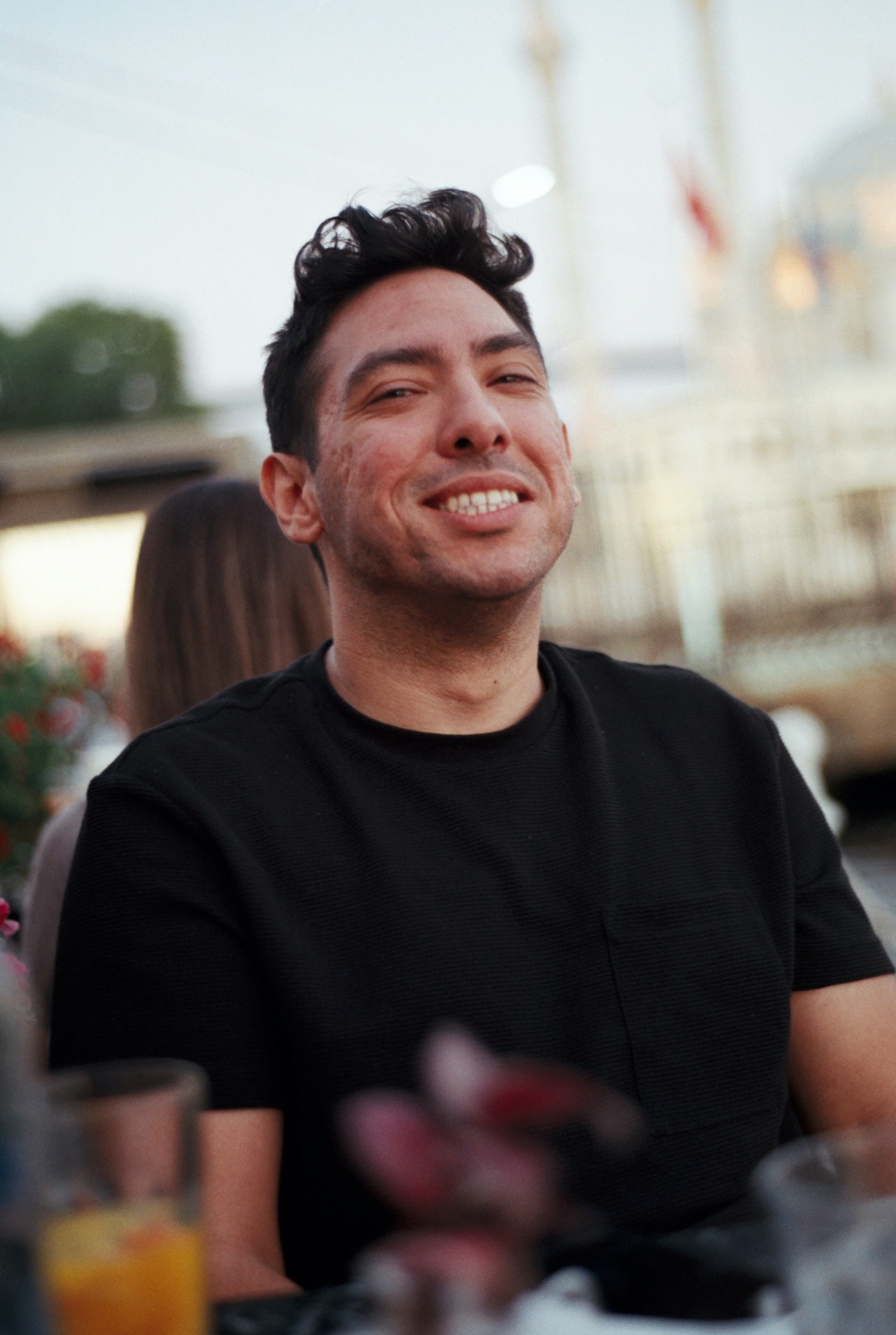 Man laughing at a café table in a black tee
