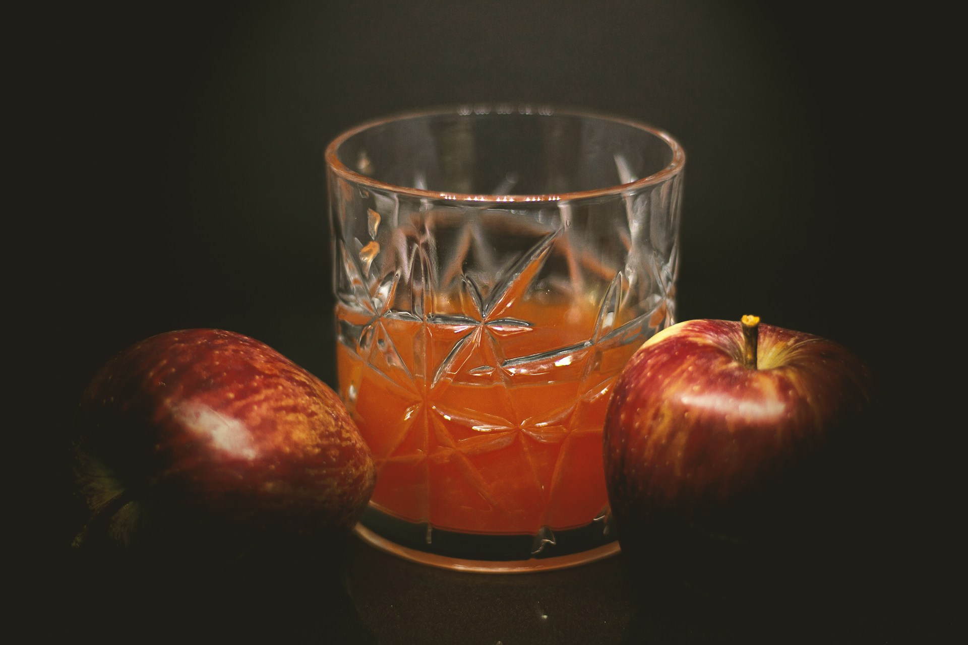 a glass filled with liquid next to two apples